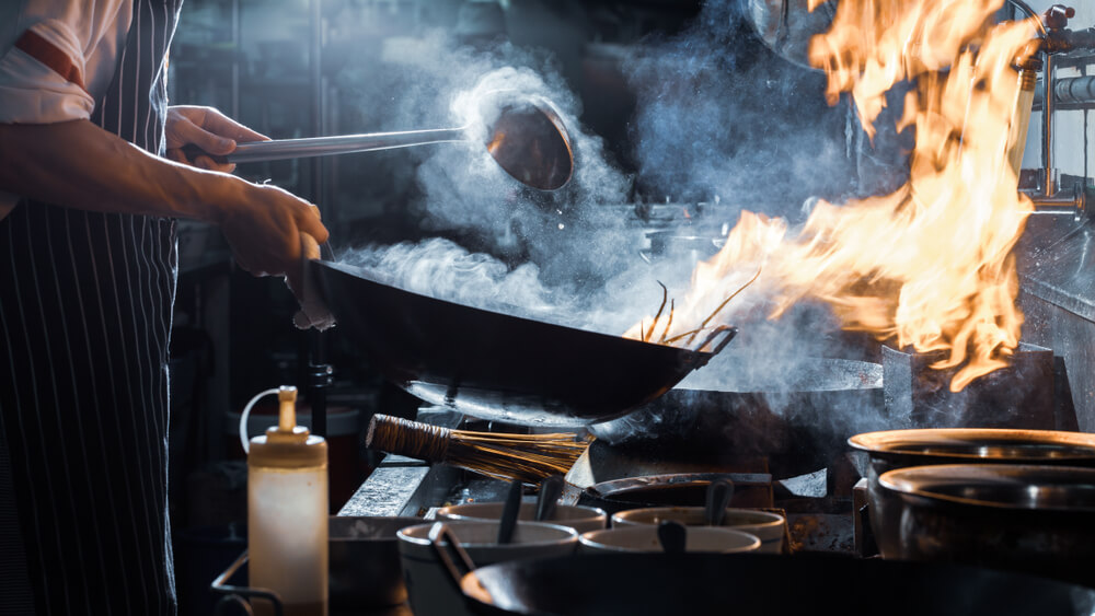 Chef cooking food in a wok pan in smokey kitchen